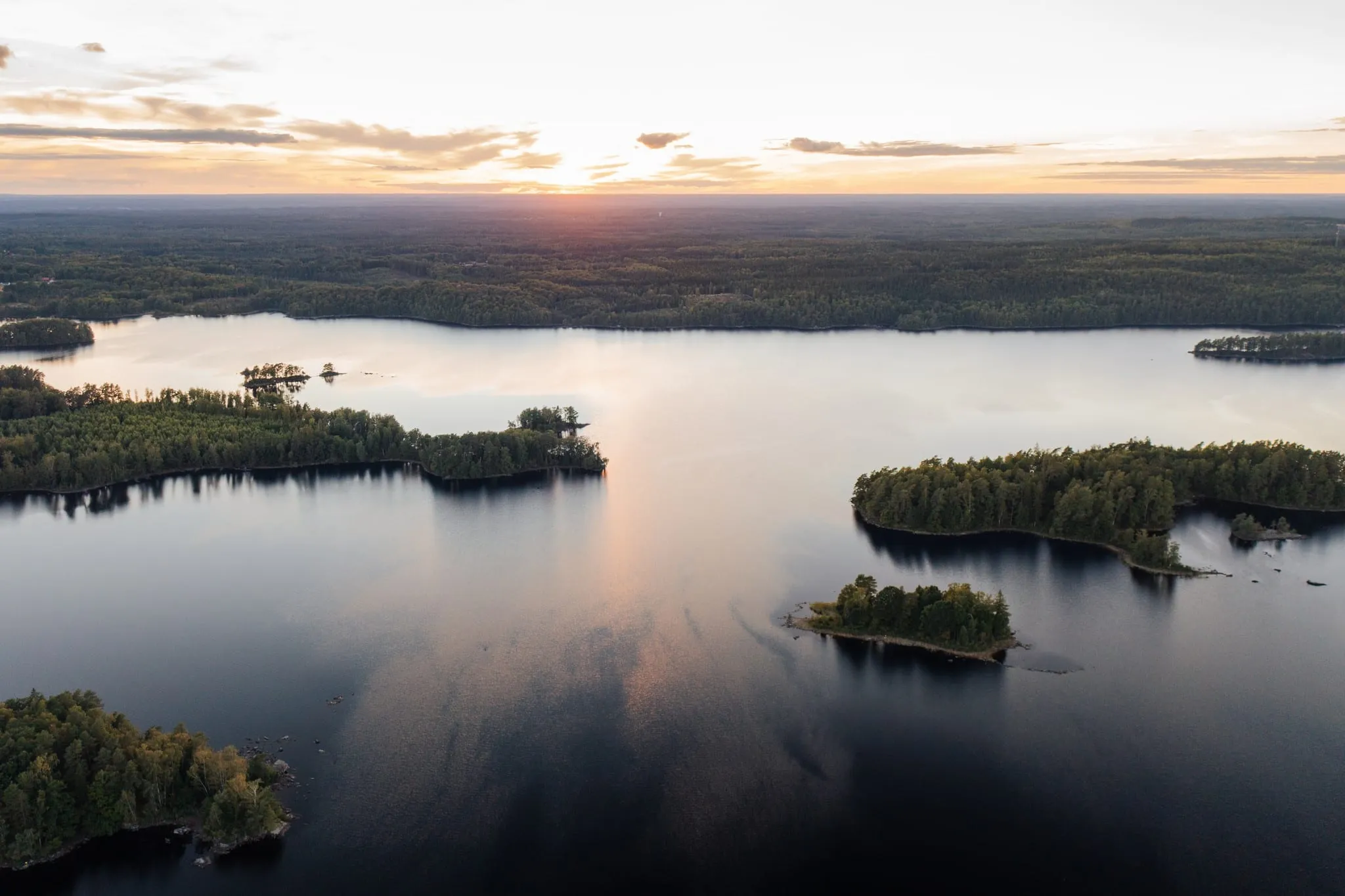 Veduta aerea di un lago con isole boscose al tramonto e la foresta fino all'orizzonte