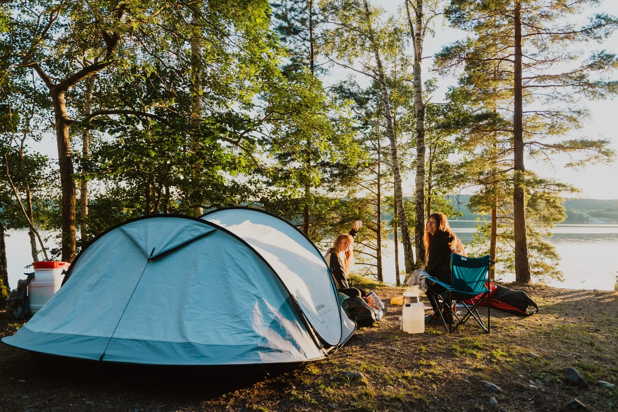 Twee kampeerders naast hun tent op een meeroever tussen de dennen