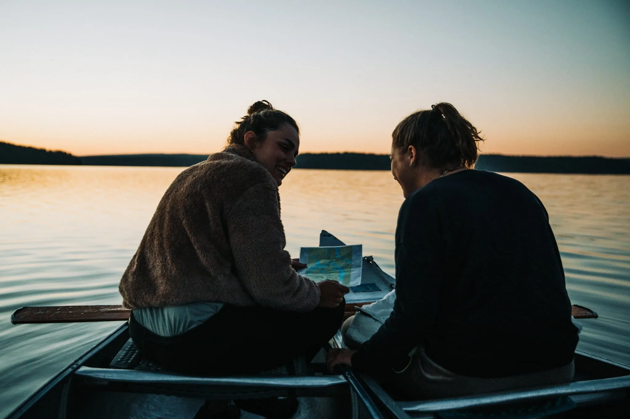 Twee kanoërs lezen een kaart in hun kano op een kalm meer bij zonsondergang