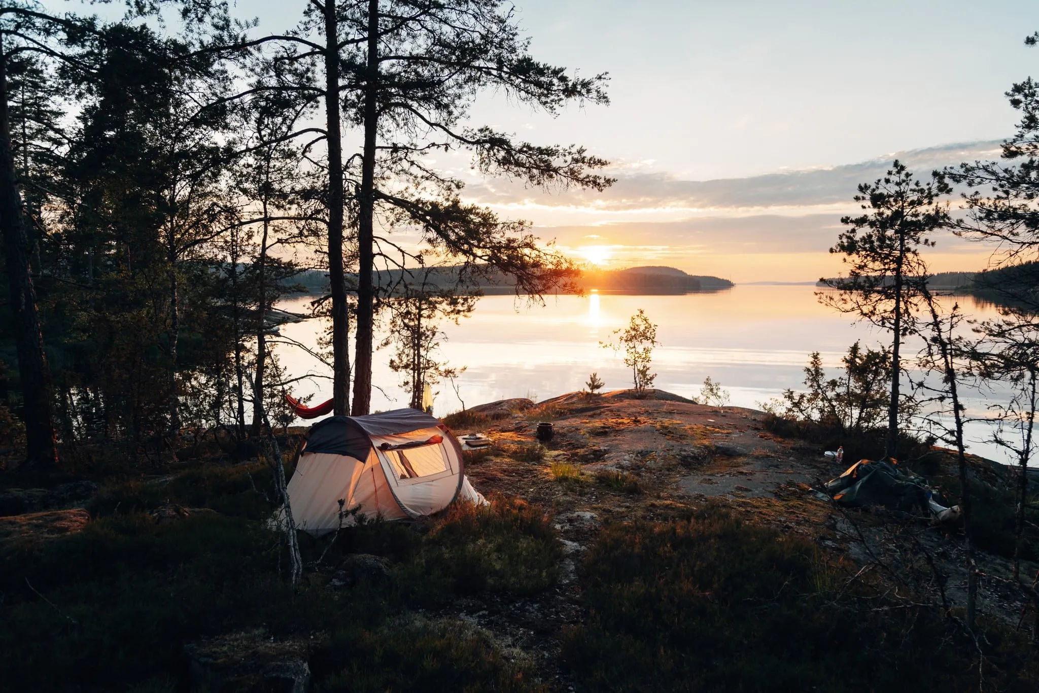 Una tenda sulla roccia nuda sopra un lago al tramonto, tra i pini